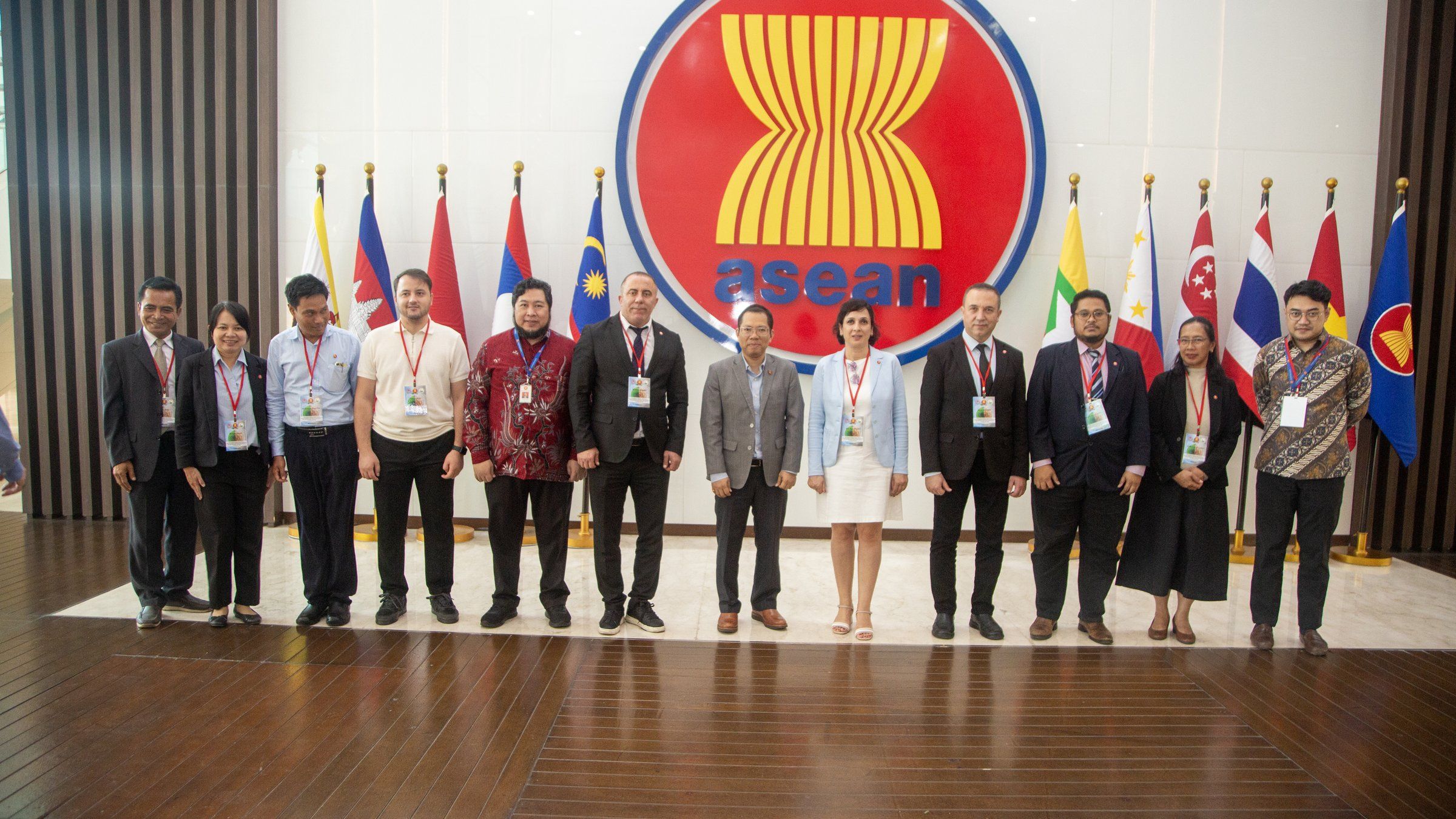 ASEAN amblemi ve üye ülke bayraklarının önünde heyet fotoğrafı